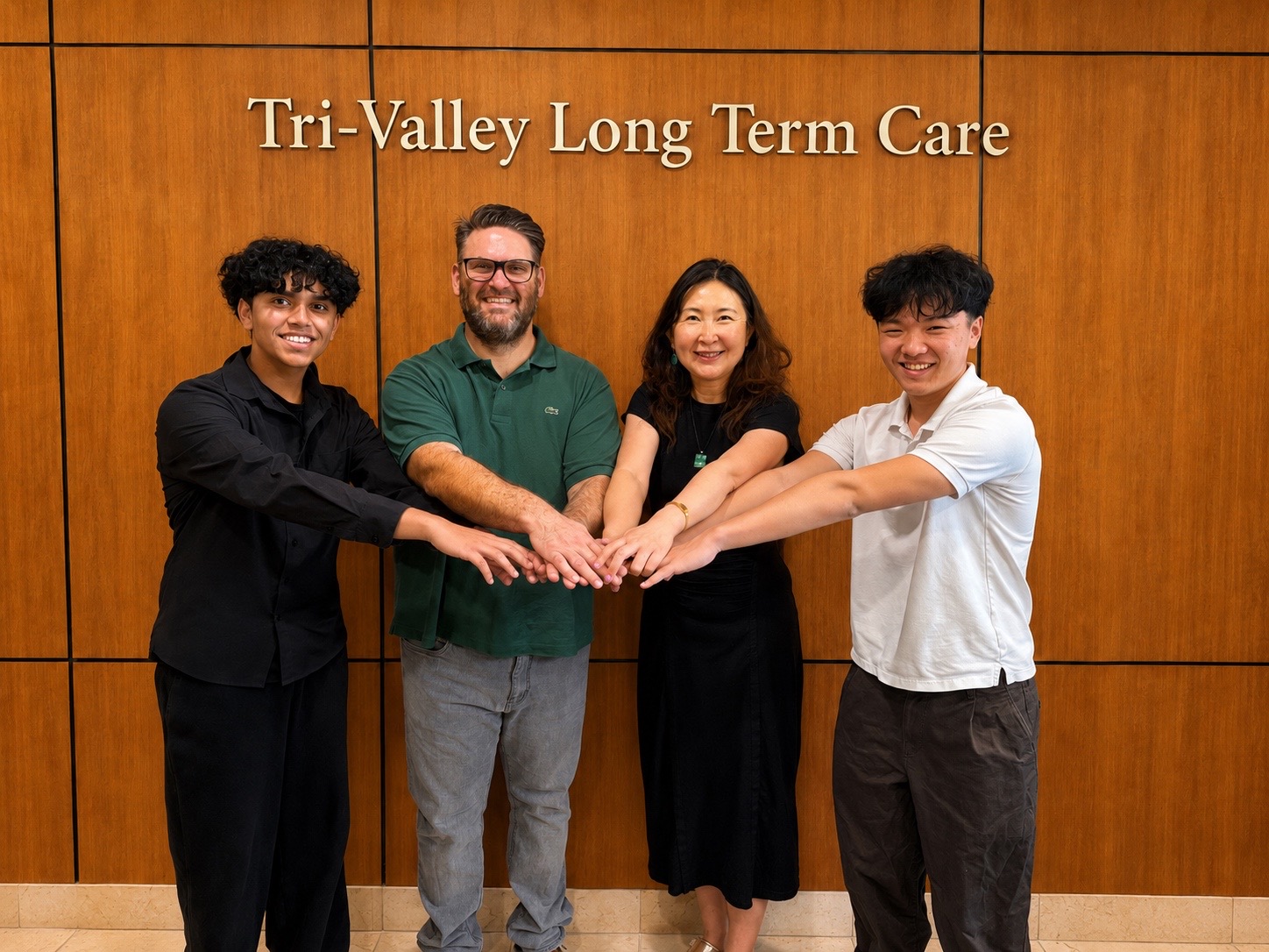 The four members of Tri-Valley Long Term Care standing side by side with their hands joined,
beneath a wall sign reading Tri-Valley Long Term Care.
